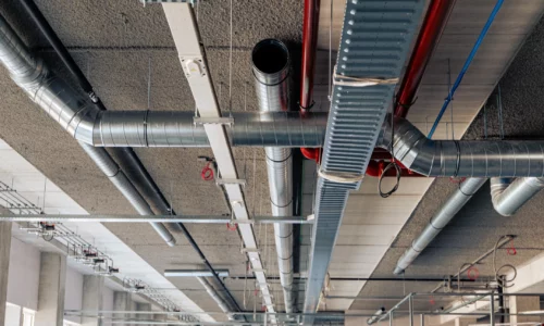 Gegalvaniseerde luchtkanalen, rode leidingen en metalen kabelgoten gemonteerd aan een industrieel plafond.