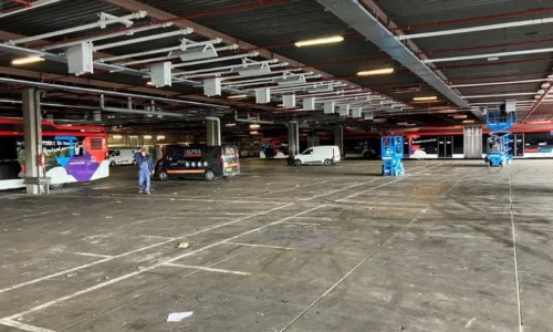 Grote overdekte busremise met geparkeerde bussen, werkbusjes en monteurs die werken met blauwe schaarliften.